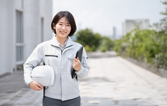 建設現場の屋外でタブレットとヘルメットを持つ作業着の女性 施工管理、現場監督のイメージ