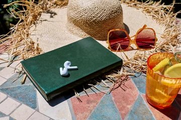 Audiobook or podcast during summer holidays. Headphones, book, rifresh drink, sunglasses and hat on white beach blanket. Summertime mood. © Caterina Trimarchi