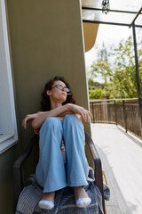 Obraz premium Relaxed woman sitting on a balcony in blue jeans and light top, sunlit outdoor space, calm mood, home life, casual comfort, peaceful self care, warm atmosphere and natural light warmth.