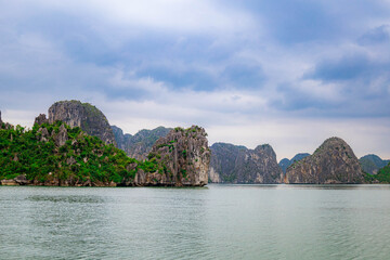 Obraz premium Beautiful tropical view of Halong bay with turquoise sea, rocky cliffs, and lush green landscape in Vietnam.