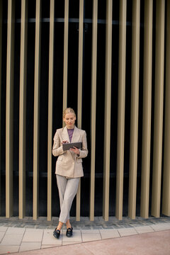 Business woman stands reading on a digital device near a striped wall