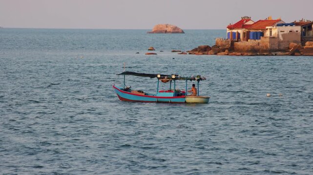 Lone fisherman sailing a traditional wooden fishing boat near the calm sea toward a rocky island with small houses. Practicing a simple and serene way of life connected to the ocean's resources