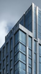 Obraz premium Modern architectural building corner with glass windows against a cloudy sky backdrop