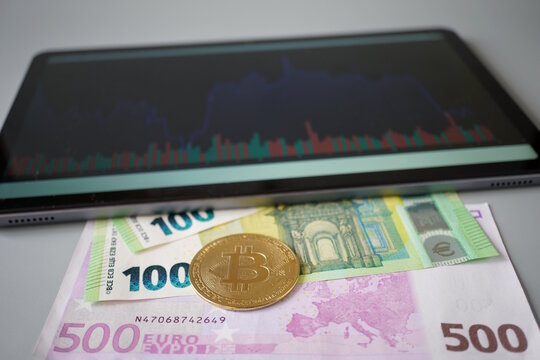 A bitcoin coin with euro notes on the background of a tablet with a chart.