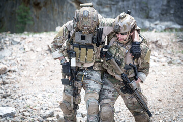 Fototapeta premium Two soldiers in tactical gear assisting each other while walking through rocky terrain