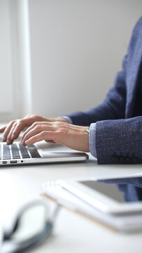 Close up of businessman's hands typing on laptop keyboard, working diligently in a modern office setting, wearing a suit and watch. Business people concept