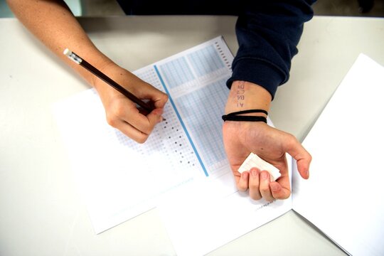 Person taking a test, writing answers on a paper with a pencil.