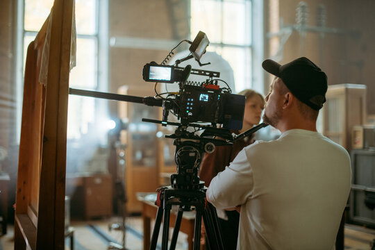 Director of photography with a camera in his hands on the set. Professional videographer at work on filming a movie, commercial or TV series. Filming process indoors, studio
