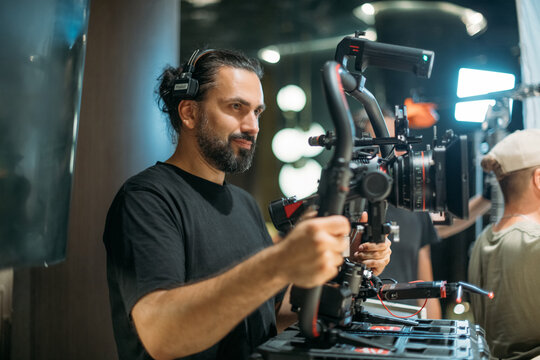 Director of photography with a camera in his hands on the set. Professional videographer at work on filming a movie, commercial or TV series. Filming process indoors, studio