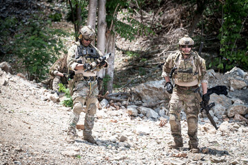 Fototapeta premium Special forces soldiers in camouflage gear with rifles in a rocky, wooded area