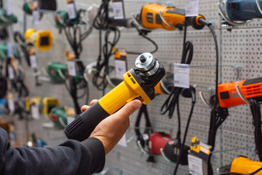 Hand holding yellow angle grinder in hardware store or power tools shop showcasing construction equipment selection and retail purchasing.
