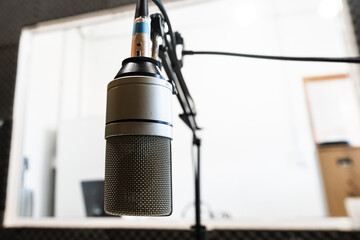 Close-up of a professional studio microphone on a boom arm with a bright, blurred control room background. © MatiasLeonel