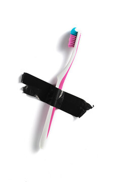 Cepillo de dientes cruzado con cinta aislante negra sobre fondo blanco. Cepillo de dientes rosa con cinta aislante negra. Concepto de prohibici&oacute;n, censura u objeto cotidiano vetado.
