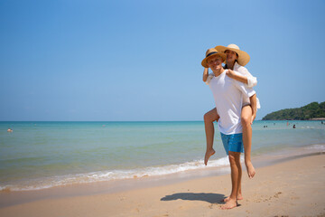 Fototapeta premium Romantic summer vacation concept. Happy young couple enjoying a piggyback ride by the tropical beach under clear blue sky, sharing love and carefree holiday mo couple, beach, 