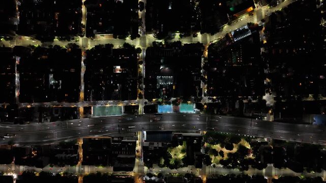 Vista cenital de una ciudad iluminada de noche con cuadr&iacute;cula de calles, manzanas, autos y tr&aacute;nsito urbano