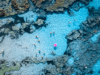 Obraz premium Aerial top down view of people swimming in crystal clear turquoise water of natural pool in rocks. Summer in Mallorca, Spain. Tourists relaxing with pink swim ring in Mediterranean sea. Drone view
