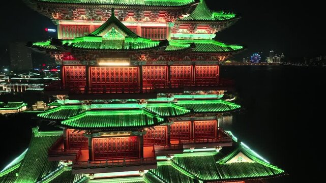 Aerial drone view of Pavilion of Prince Teng illuminating the night while reflecting multiple times across a dark lake, showcasing the intricate architecture of this historic Nanchang landmark