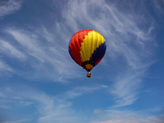 Obraz premium Colorful hot air balloon flying in blue sky with wispy clouds 