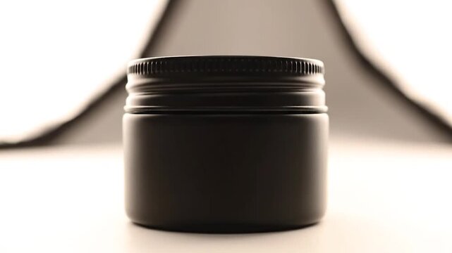 Matte black cosmetic jar mockup with screw lid on neutral background