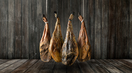 Piernas de jamón ibérico colgadas sobre un fondo rústico de madera oscura. Tradicional jamón ibérico español colgado sobre madera oscura. Concepto gastronómico, rústico y auténtico.