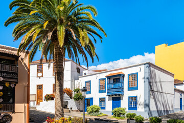 Fototapeta premium Charming cobblestone plaza is lined with white traditional buildings featuring bright blue wooden accents in Santa Cruz town, La Palma, Canary Islands, Spain