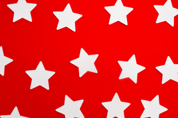 Fototapeta premium White paper stars pattern on bright red background surface top view. Flat lay composition of clean star shapes evenly distributed over vibrant colorful backdrop.