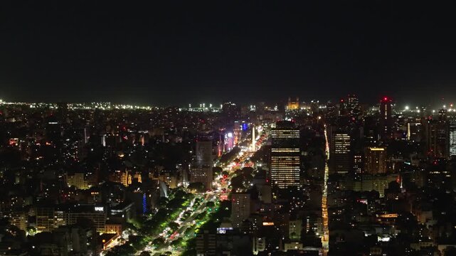 Vista a&eacute;rea nocturna con dron de la ciudad de Buenos Aires sobre la Avenida 9 de Julio y el Obelisco iluminado con tr&aacute;nsito urbano. Turismo, paisajes, porte&ntilde;o, ciudad magica.