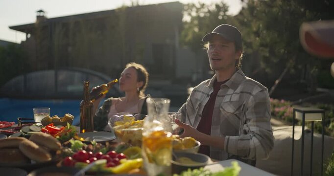 Relaxed backyard dinner by the pool at sunset with food, drinks, and casual conversation