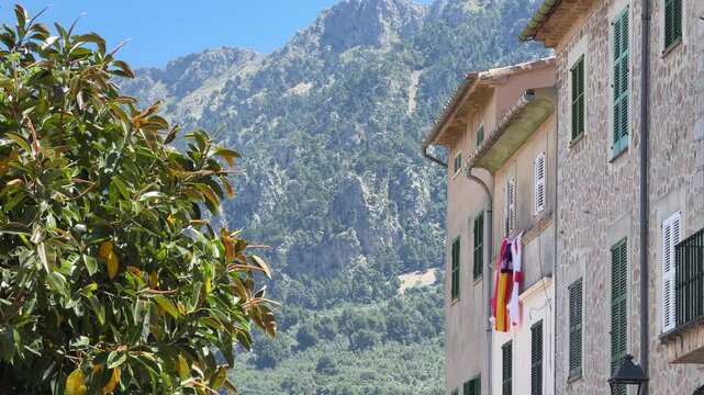 Charming street in Soller, Mallorca, framed by traditional stone buildings and lush greenery, with the dramatic Tramuntana mountains rising in the background.