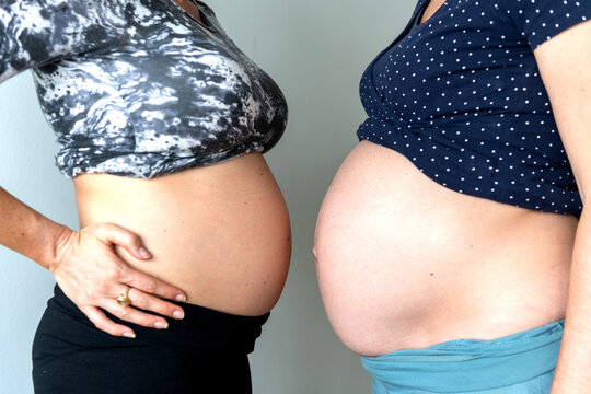 Two pregnant women standing side by side, showing their bellies.