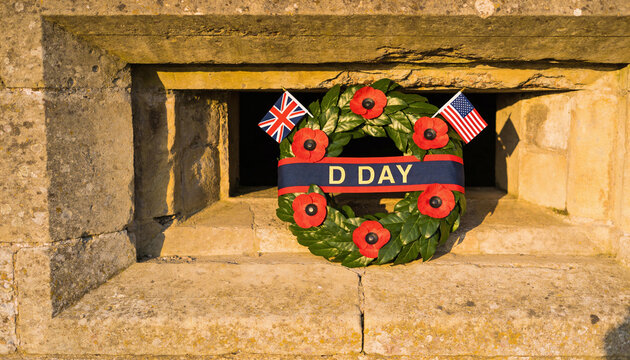 D-Day memorial wreath with red poppies and flags in a stone bunker embrasure.
