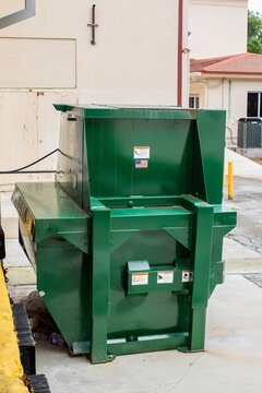 Small industrial green trash compactor in back of building