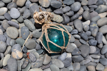 Vintage Japanese glass fishing floats and smooth gray pebbles piled together on a sandy beach by the ocean shore © Devka