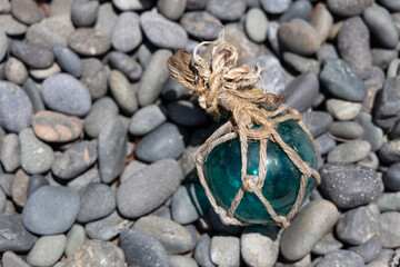 Vintage Japanese glass fishing floats and smooth gray pebbles piled together on a sandy beach by the ocean shore © Devka