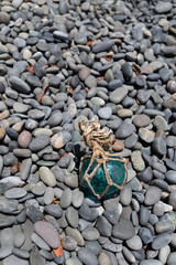 Vintage Japanese glass fishing floats and smooth gray pebbles piled together on a sandy beach by the ocean shore © Devka