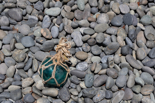 Vintage Japanese glass fishing floats and smooth gray pebbles piled together on a sandy beach by the ocean shore