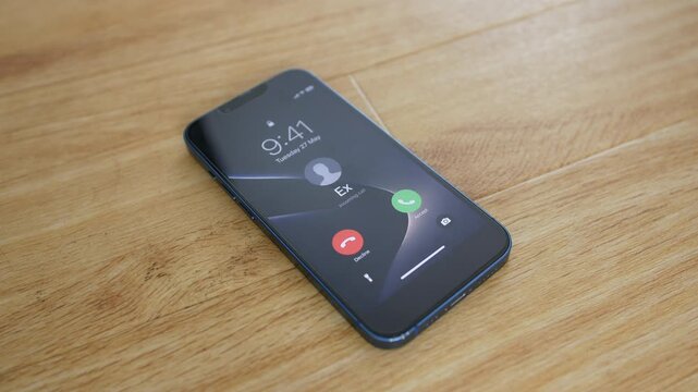 Phone displaying an incoming call from Ex rests on a wooden surface. Close-up mobile, cell, smartphone view highlights ex partner, ex lover, breakup, former relationship, caller ID, communication