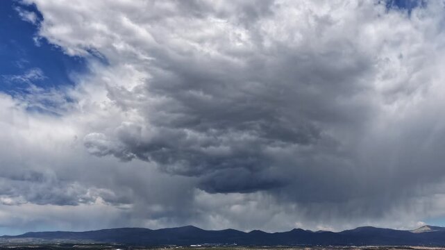 Aerial drone timelapse capturing an intimidating monsoon storm. Heavy dark clouds swirl and form dynamically, unleashing powerful localized rain showers over a rugged mountain landscape.