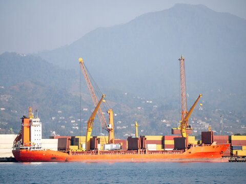 Cargo ship loading containers at seaport terminal with harbor cranes for global freight logistics and international maritime trade.