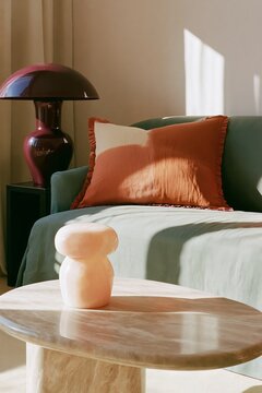 Living room corner featuring a deep sage linen sofa with an orange decorative pillow, a marble coffee table, and a modern lamp casting soft light