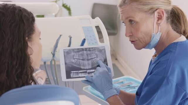 Doctor dentist and woman patient watching x-ray on digital tablet