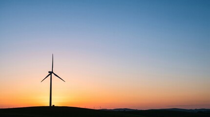 Obraz premium Silhouette of a wind turbine against a gradient sunset sky with rolling hills