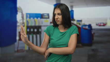 Woman pushes hands away and turns head with a disgusted look near a fuel pump at a petrol station building  disgust refusal boundary. © Krakenimages.com