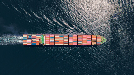 Fototapeta premium Container vessel carrying numerous shipping containers across the open sea, symbolizing global trade, international logistics, and maritime transportation, seen from a high aerial perspective