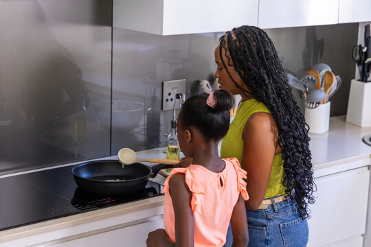 African American mother and teenage daughter cooking at stovetop at home with frying pan, ladle