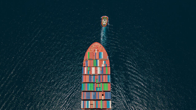Container ship navigating through deep blue ocean with a tugboat trailing behind, representing global logistics, transport, and international trade supply chain operations