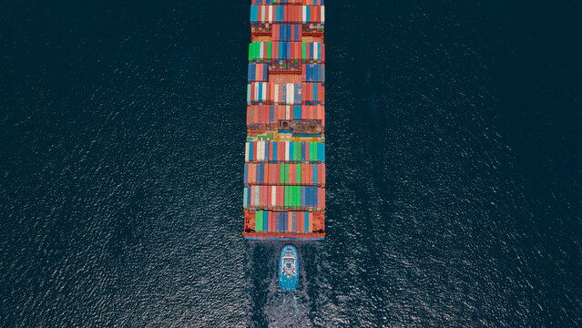Aerial view showing a large dredge barge with a crane and tugboats working in the water, actively moving sand to expand a beach or landmass, highlighting coastal construction