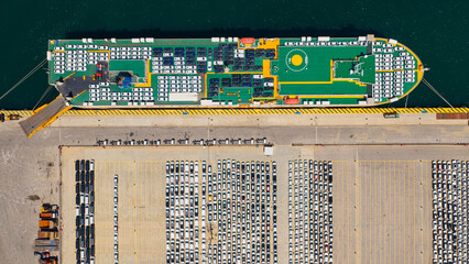 Fototapeta premium Car carrier ship docked at an industrial port, actively loading and unloading new vehicles for global distribution across the modern automotive logistics infrastructure
