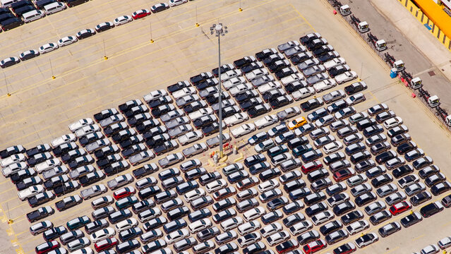 Rows of new automobiles parked at a large industrial lot awaiting transport, highlighting global supply chain operations and vehicle distribution at a busy port terminal