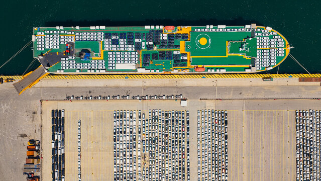 Car carrier ship docked at an industrial port, actively loading and unloading new vehicles for global distribution across the modern automotive logistics infrastructure